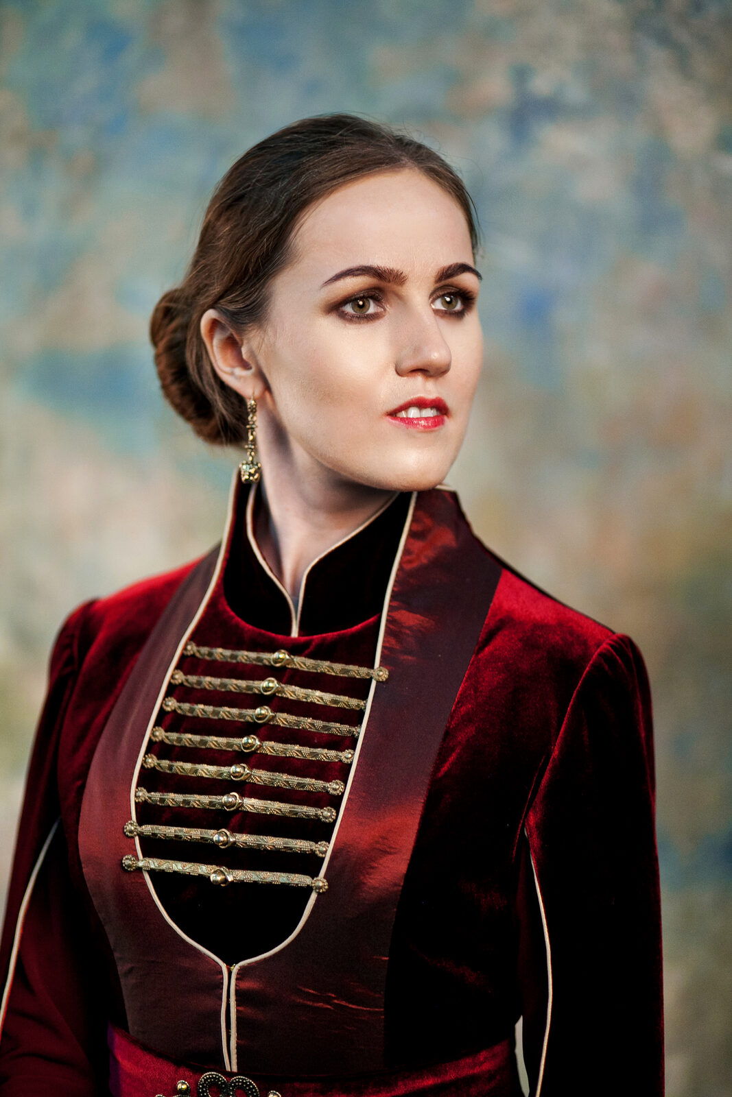 A close, bust-length portrait of Nafset in traditional Circassian dress, turned slightly to the side with her gaze toward the camera. The photo shows the dress’s chest fastenings in detail — rows of decorative gold buckles running down each side of the chest over a black underlay, with a stand collar at the neck.